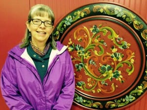 Jill Williams stands with traditional Norwegian rose mauling design piece. Photo/Angela Denning