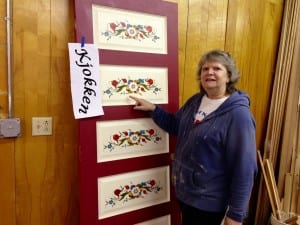 Sally Dwyer points to one of the new doors decorated with rose mauling at the Sons of Norway hall. Photo/Angela Denning