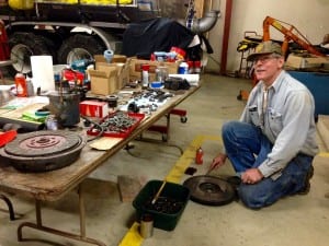 Jack Slaght kneels next to a work table covered in parts for the 1936 International fire truck. Photo/Angela Denning