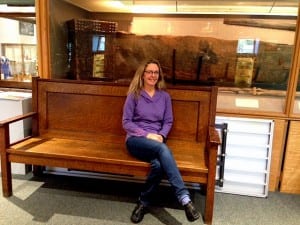 Museum Director, Kathi Riemer, sits in front of a display featuring an undated bentwood box. Photo/Angela Denning