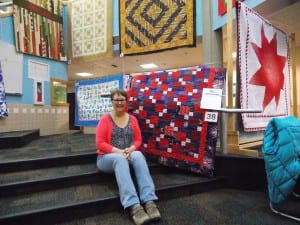 Carol Kandoll sits next to a Quilt of Valor at the quilt show in the Petersburg High School lobby, Oct. 22. Photo/Angela Denning
