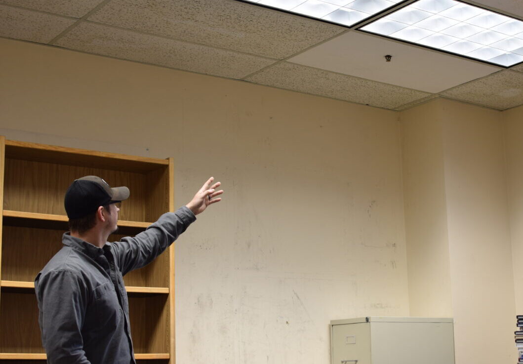 Aaron Buller points at a fire sprinkler head in a damaged, emptied out office.