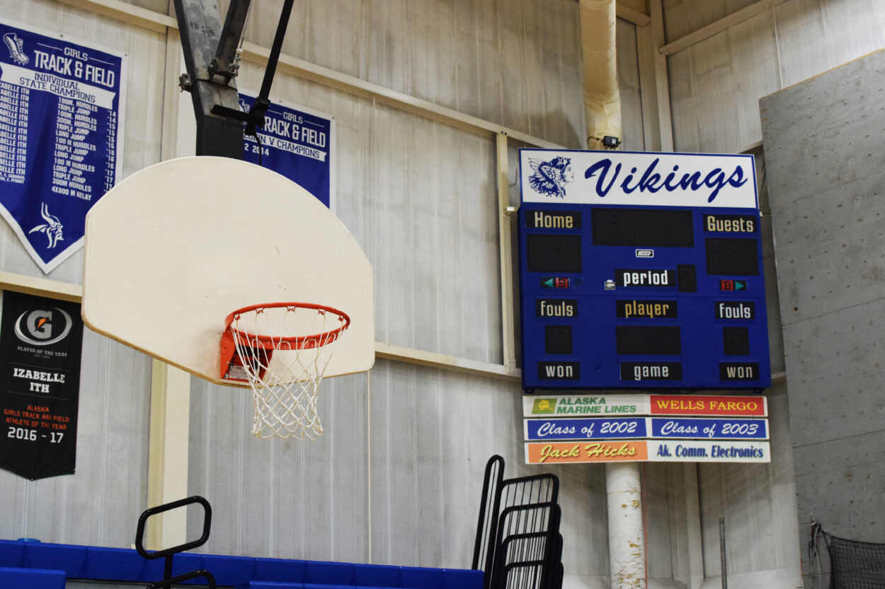 A basketball hoop in the Petersburg High School gymnasium. An unlit scoreboard hangs to the right of the hoop.