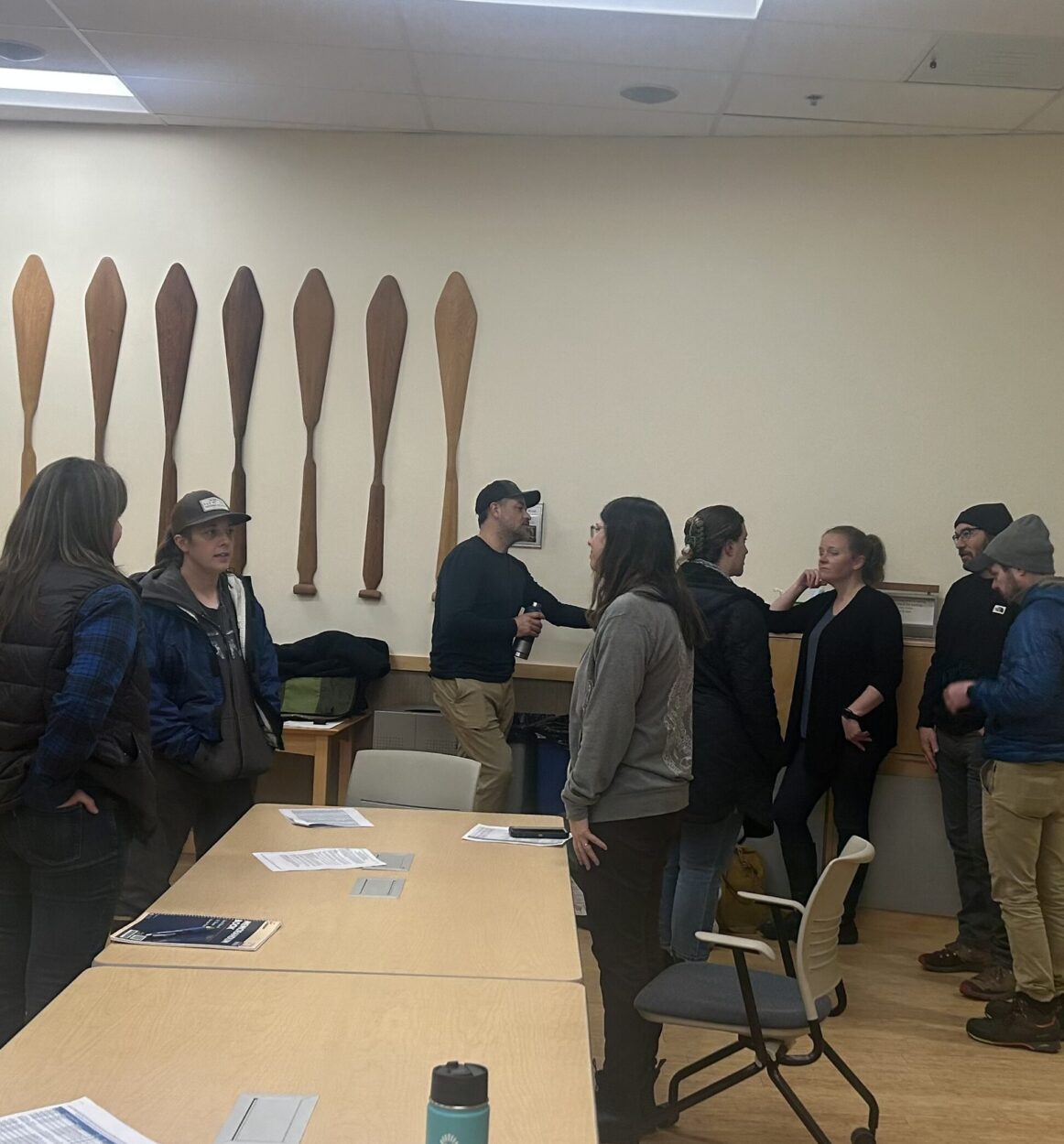 A group of nine people gather in front of a table with pamphlets scattered around the surface. 