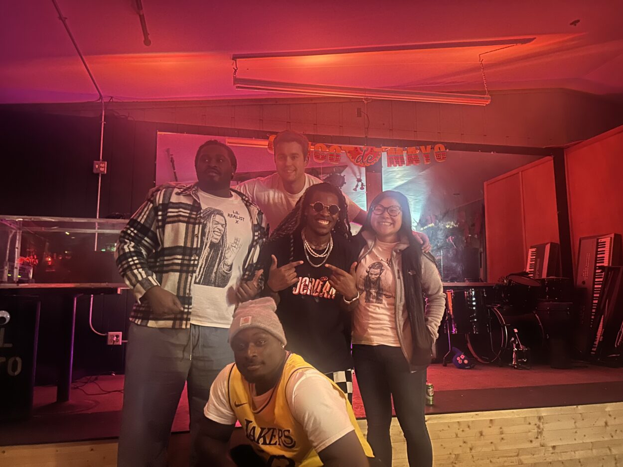 Little Realist X poses in front of a small stage, surrounded on all sides by four friendss.