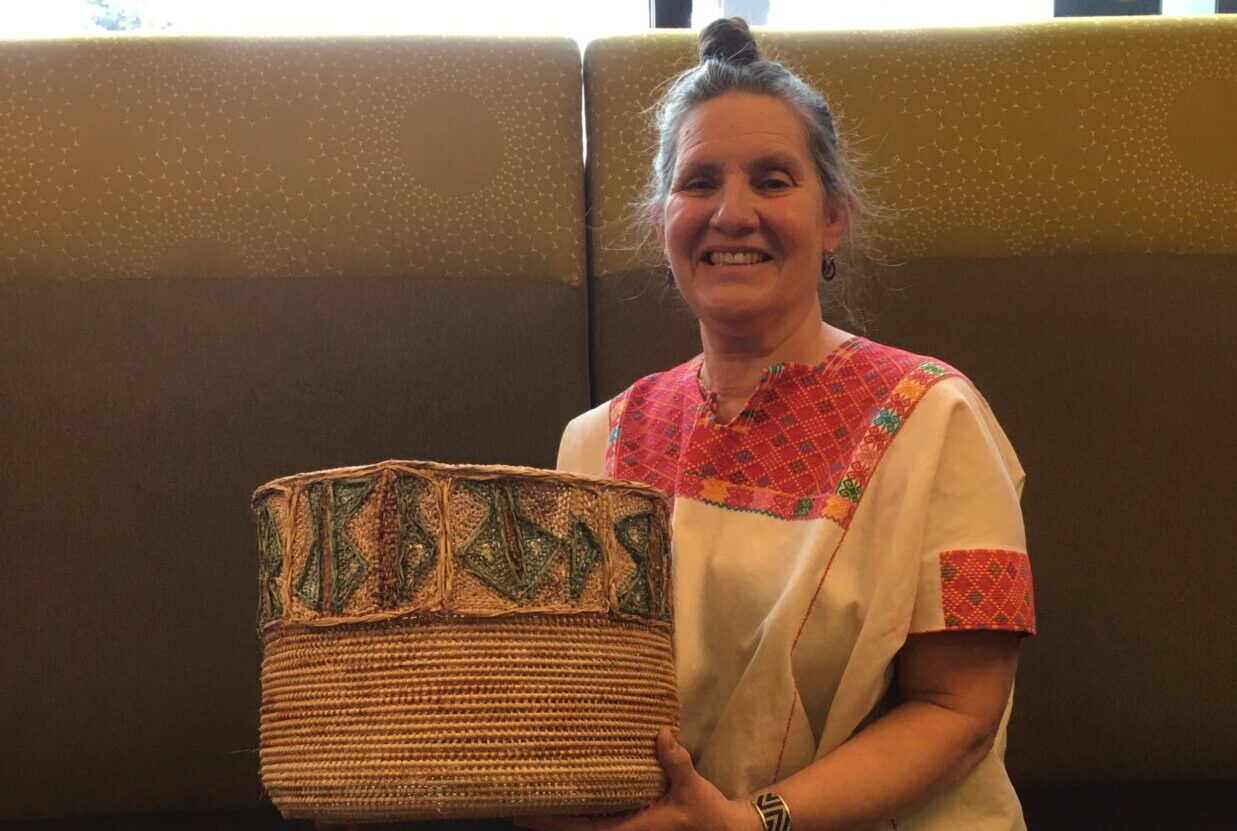 Kathy Rousso is sitting on a high-backed couch with a large basket. She is smiling.
