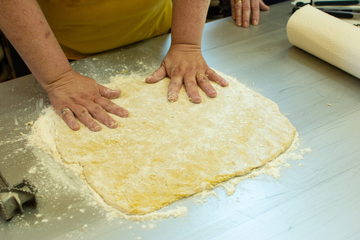 The hands of Samantha Wikan-Williams flattening a sheet of dough onto a metal table.