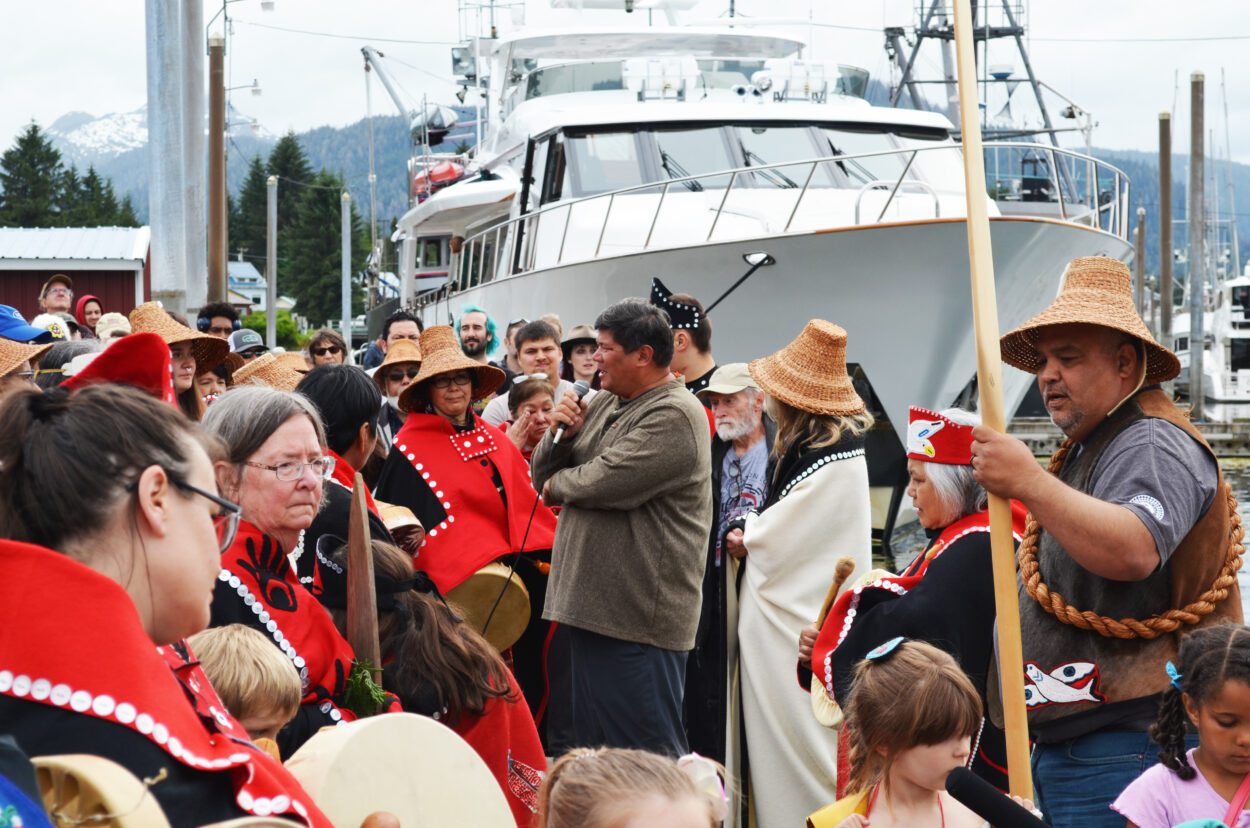 Mark Ellis stands in front of a crowd of people wearing Lingít regalia at Petersburg's South Harbor.