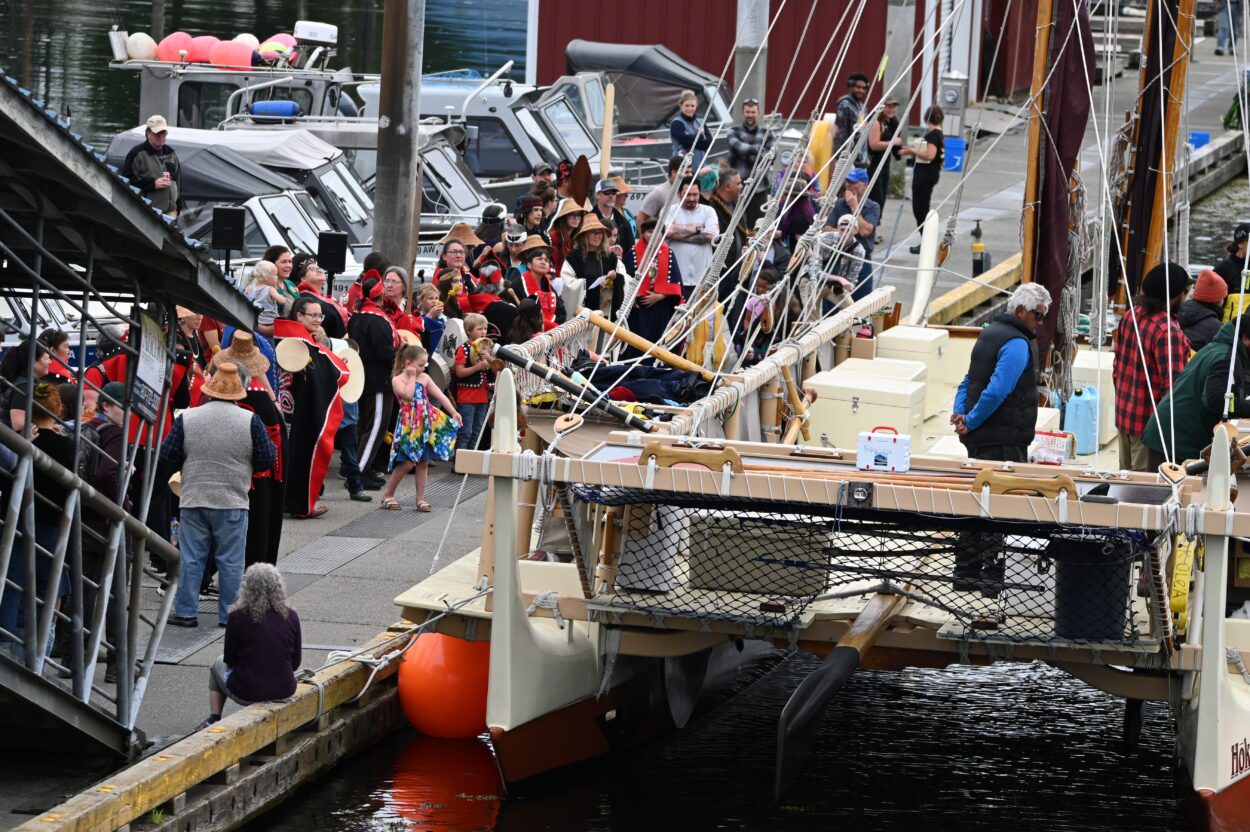 A crowd of people dressed in Lingít regalia line the docks and ramp of Petersburg's South Harbor as the crew of the Hōkūleʻa tie up.