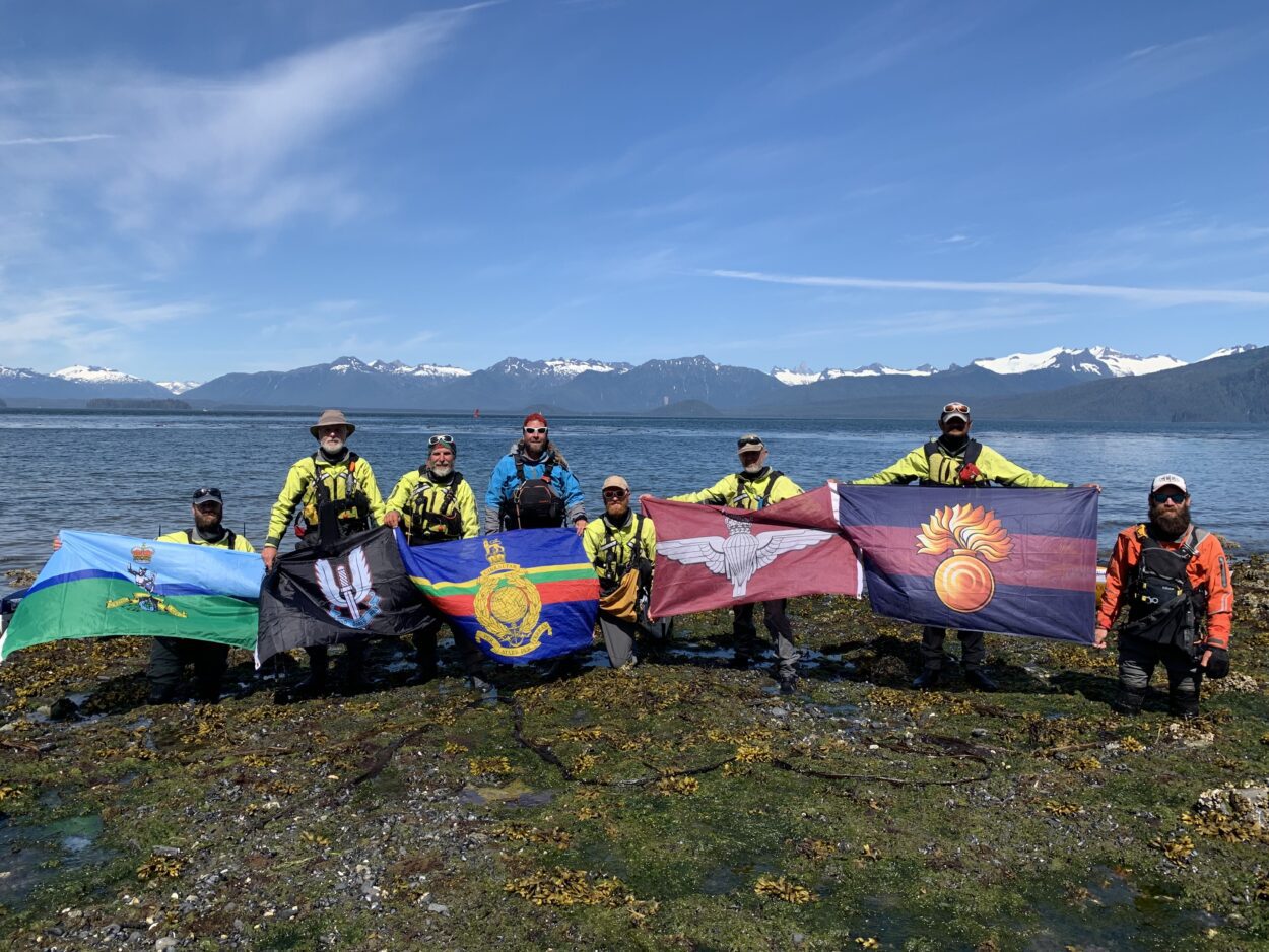 Eight men kneeling on a beach raising flags.