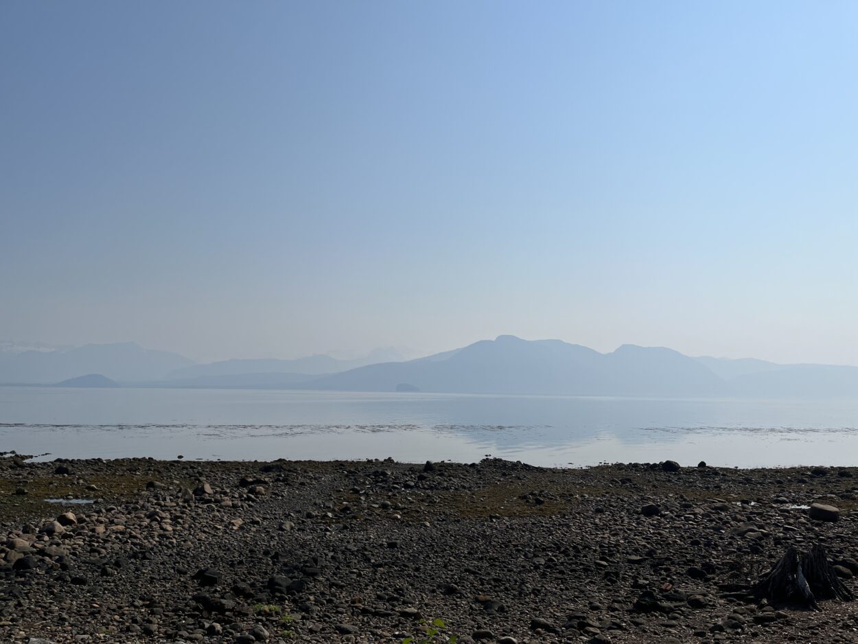 The coastline of Sandy Beach on a sunny day. Only a few mountains are visible in the distance. They're half-obscured by a thick fog.  