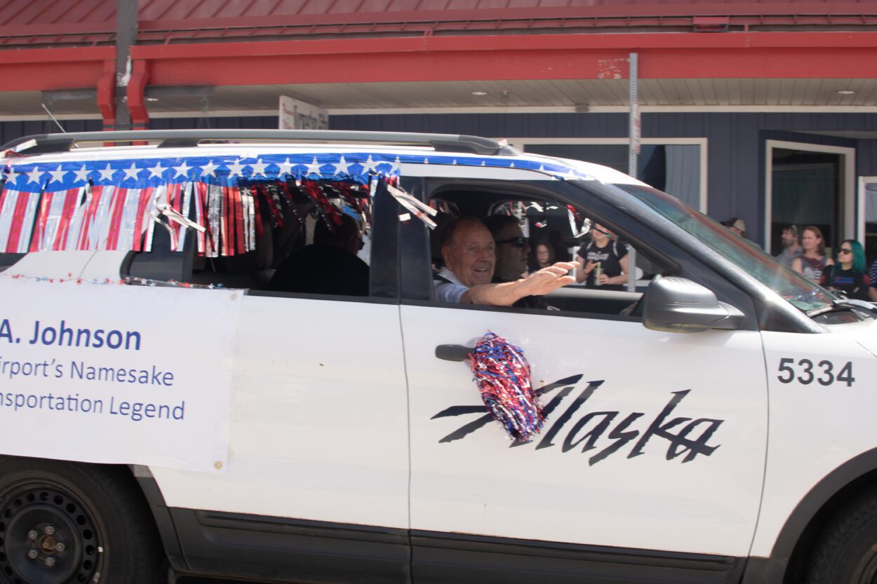 James A. Johnson riding in the passenger seat of an Alaska Airlines van decorated with red white and blue streamers.