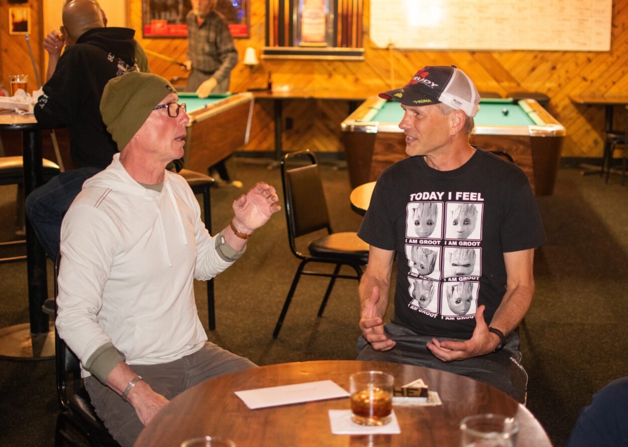 Andrew Simmonds and Scott May speaking to each other at a table in a bar. There are drinks on the table in front of them.